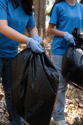 Up close, a group of Asian volunteers collects trash in plastic bags and cleans areas in the forest to preserve the natural ecosystem.