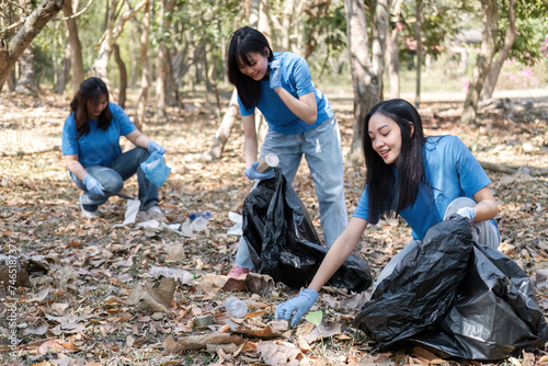 A group of Asian volunteers collects trash in plastic bags and cleaning areas in the forest to preserve the natural ecosystem.