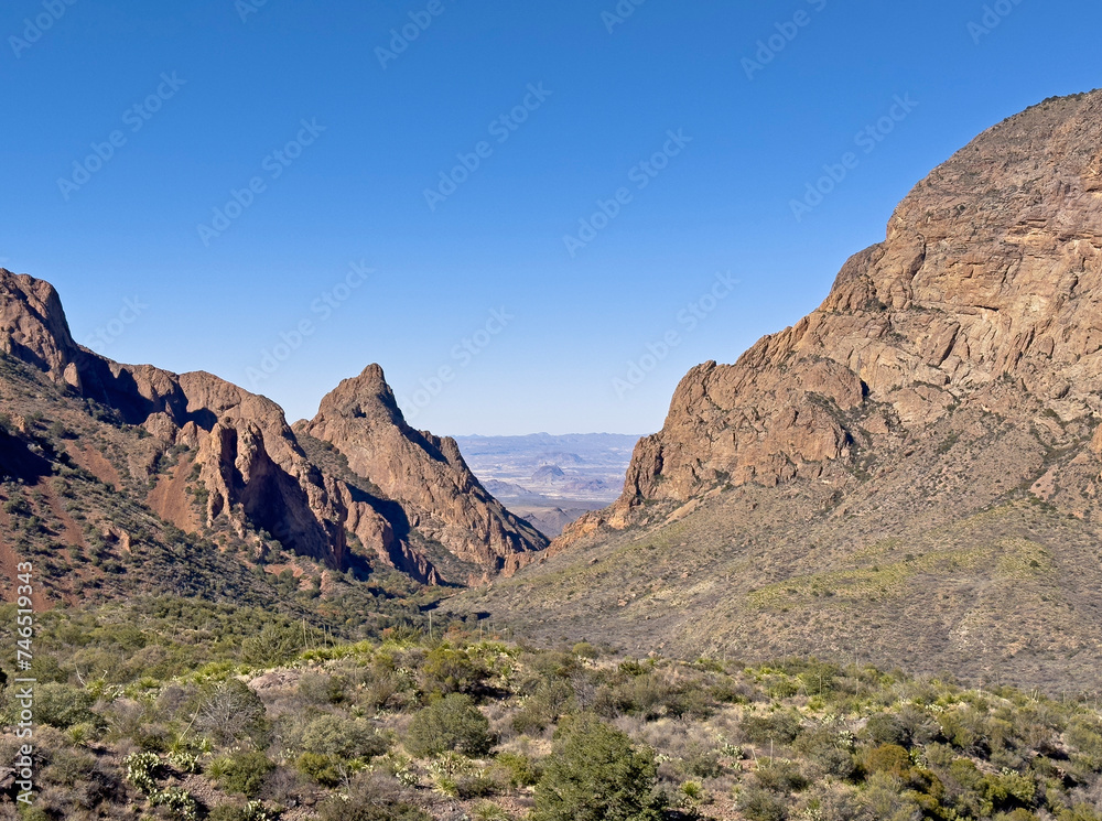 A desert valley in between two mountains and rock formations in Big Bend National Park in Texas. This landscape has a narrow view and clear blue skies for a remote Southwest destination.