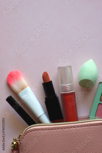 Pink make up bag with various beauty products. Pink background, top view.