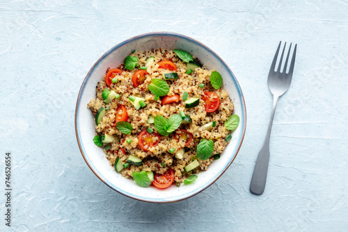 Quinoa tabbouleh salad in a bowl, a healthy dinner with tomatoes and mint, overhead flat lay shot with a fork