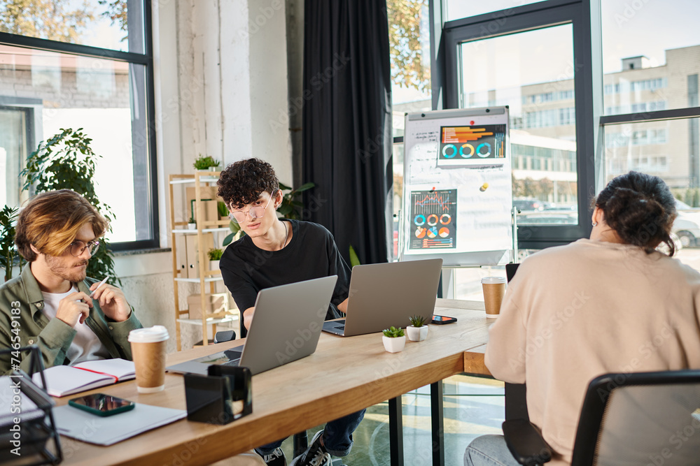 Young professionals in their 20s sharing ideas near laptops in a coworking space, charts