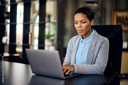 A focused African businesswoman, typing an email, sending to some clients, working at her office.