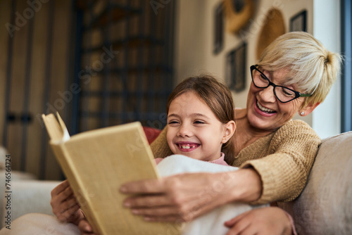 A lovely smiling grandma and her grandchild, reading a book together, sitting on the couch. photo