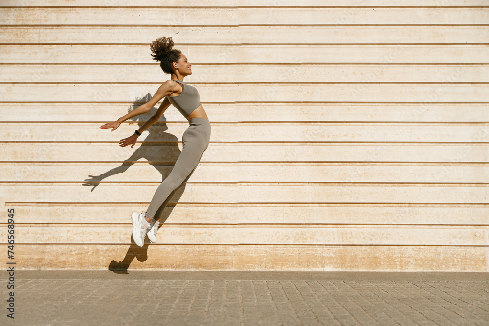Young fit woman in sportswear leaping in the air with wall backdrop outdoors. High quality photo Young fit woman in sportswear leaping in the air with wall backdrop outdoors. High quality photo
