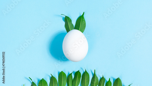 White chicken egg decorated with natural green leaves, symbol of Easter Bunny. Ears move cyclically. Row of leaves below is symbolizing lawn. photo