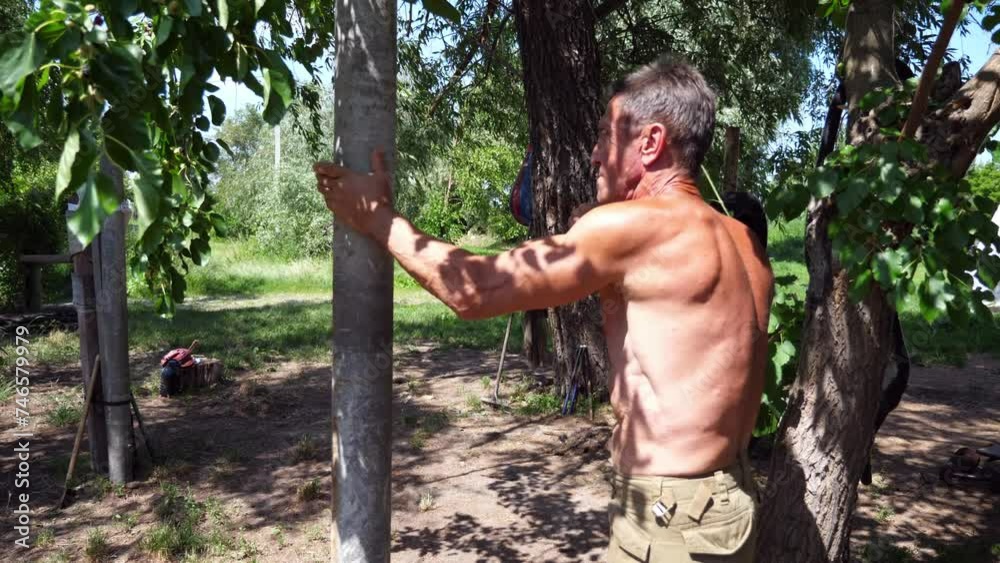 An adult male athlete showing fighting techniques on a wooden dummy outdoor. Older sportsman exercising martial arts at summer day. Old man practicing a wing chun kung fu. Concept of healthy lifestyle An adult male athlete showing fighting techniques on a wooden dummy outdoor. Older sportsman exercising martial arts at summer day. Old man practicing a wing chun kung fu. Concept of healthy lifestyle