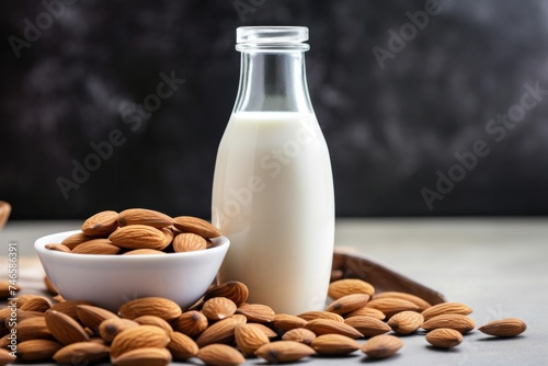 Milk in glass bottle near ceramic bowl with raw almonds on stone table in kitchen