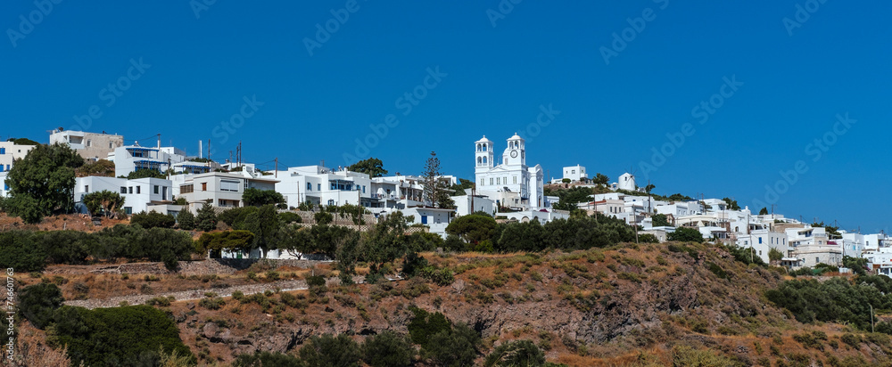 bell and clock tower of typical Greek Orthodox church, whitewashed building in sunlight on blue sky in tiny greek village tripity