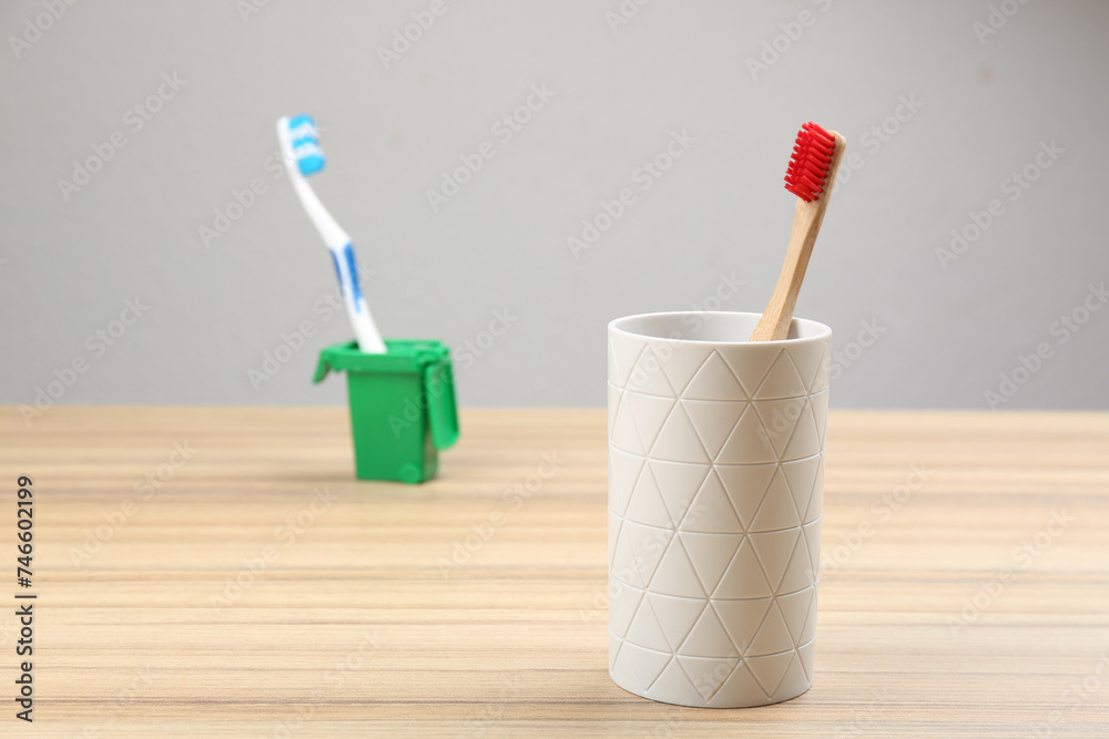 Natural bamboo toothbrush and plastic one in toy trash can on wooden table Natural bamboo toothbrush and plastic one in toy trash can on wooden table