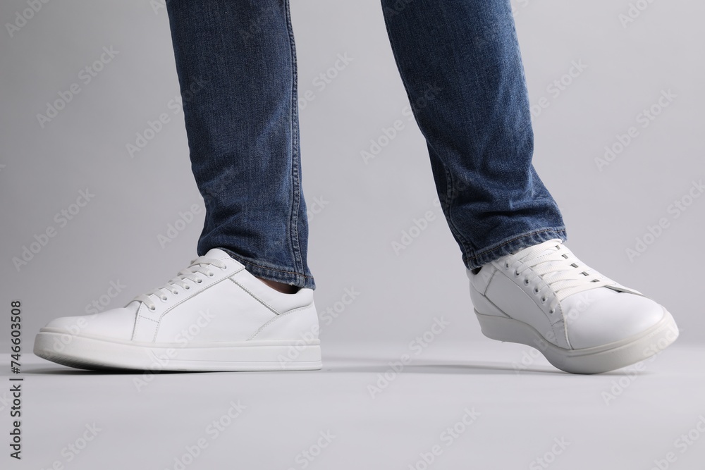Man wearing stylish white sneakers on grey background, closeup Man wearing stylish white sneakers on grey background, closeup