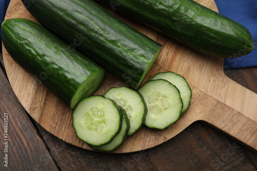 Fresh whole and cut cucumbers on wooden table, top view