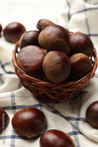 Sweet fresh edible chestnuts in wicker bowl on table, closeup