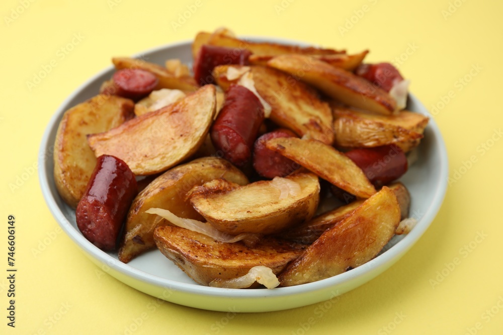Delicious baked potato with thin dry smoked sausages and onion on yellow table, closeup
