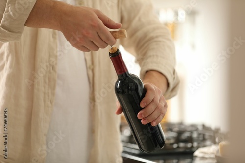Man opening wine bottle with corkscrew indoors  closeup