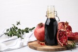 Tasty pomegranate sauce in bottle, branches and fruits on light table, closeup. Space for text