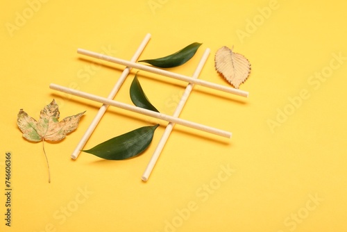 Tic tac toe game made with fresh and dry leaves on yellow background, space for text