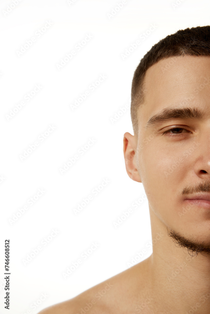 Fototapeta premium Half-portrait of confident young man looking at camera with light smile against white studio background. Concept of beauty procedures, male health, body care, spa treatment, hygiene. Ad