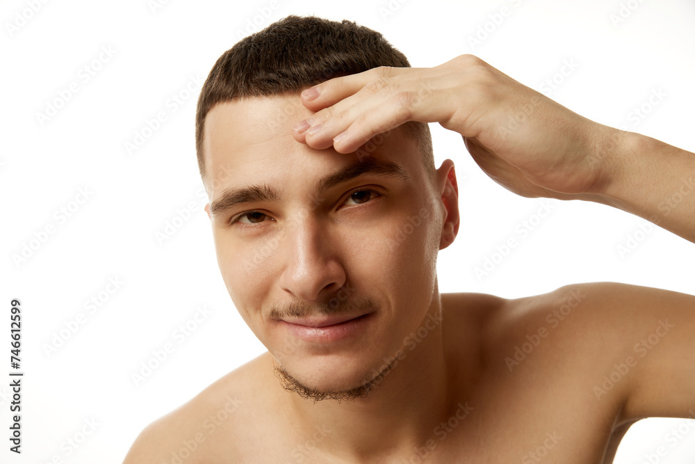 Bare-chested man with neat beard and haircut, placing fingers on his temple, looking contemplative against white studio background. Concept of beauty, male health, body care, spa treatment, hygiene. Bare-chested man with neat beard and haircut, placing fingers on his temple, looking contemplative against white studio background. Concept of beauty, male health, body care, spa treatment, hygiene.