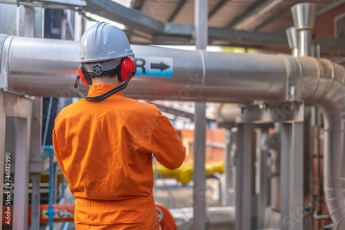 Young engineer working at large factory,Technician in protective uniform and with hardhat checking temperature in pipes