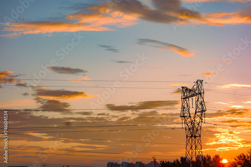 A high-voltage power tower and urban skyline set against the backdrop of a brilliant morning sunrise and sunset