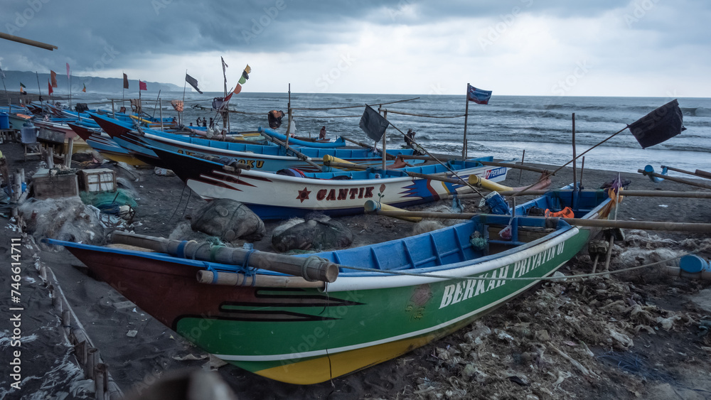 Fishing boats are lined up along the beach, as they refrain from heading out to sea due to cloudy weather and the imminent threat of heavy rain