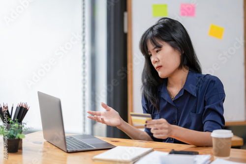 Stressed Asian businesswoman looking at laptop screen while holding credit card and facing transaction problems