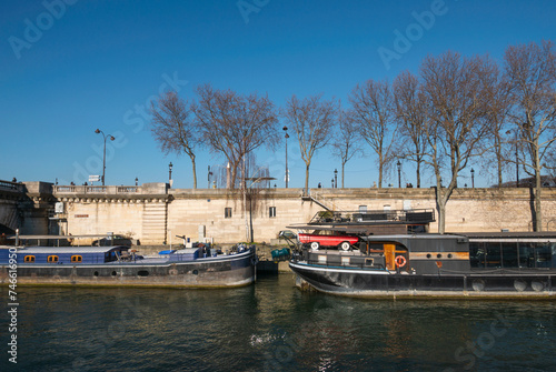 two boats - barges - behind each other on river Seine in Paris France with riverbank and car and trees photo