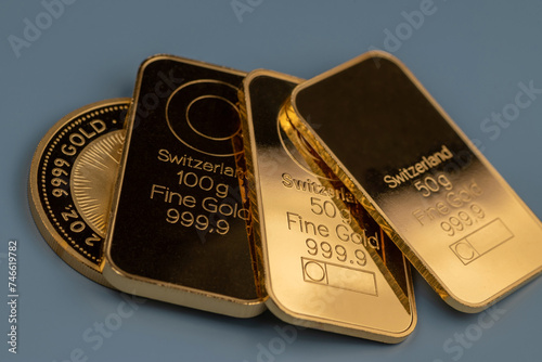 Gold bars and gold coin on a blue grey background. Selective focus.
