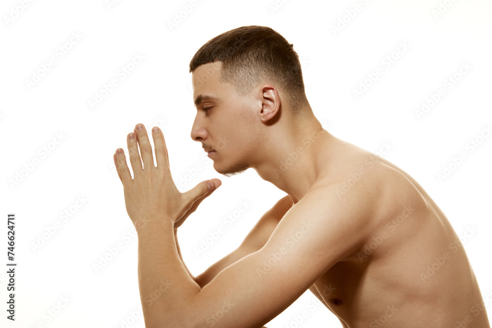 Side view of thoughtful shirtless man with serious and focused expression folded his hands together against white studio background. Concept of procedures, male health, body care treatment, hygiene. Side view of thoughtful shirtless man with serious and focused expression folded his hands together against white studio background. Concept of procedures, male health, body care treatment, hygiene.