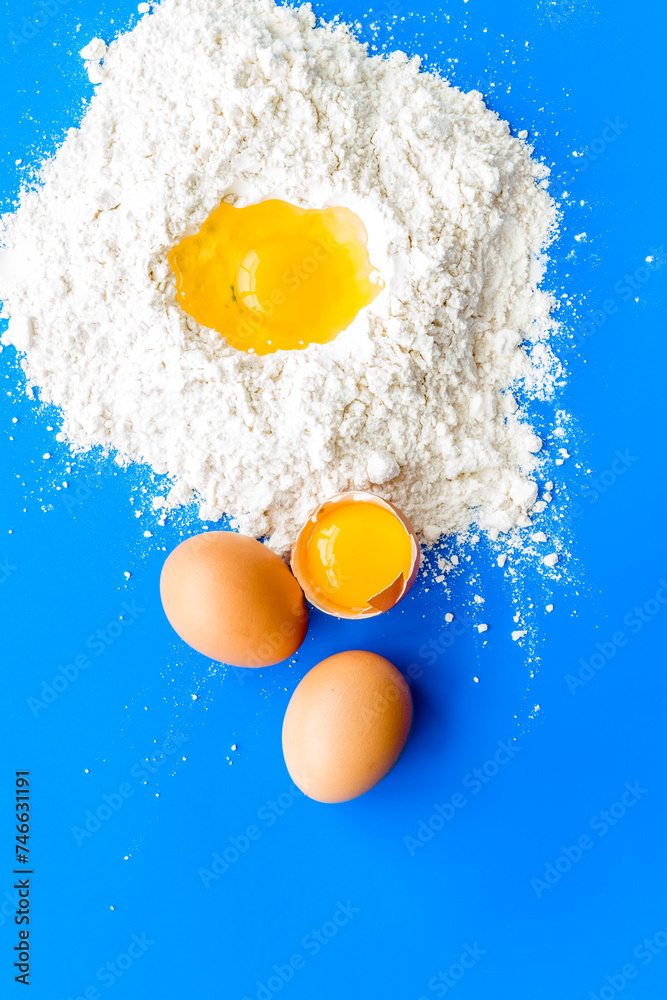 Making dough concept. Pile of flour and eggs on blue background top view