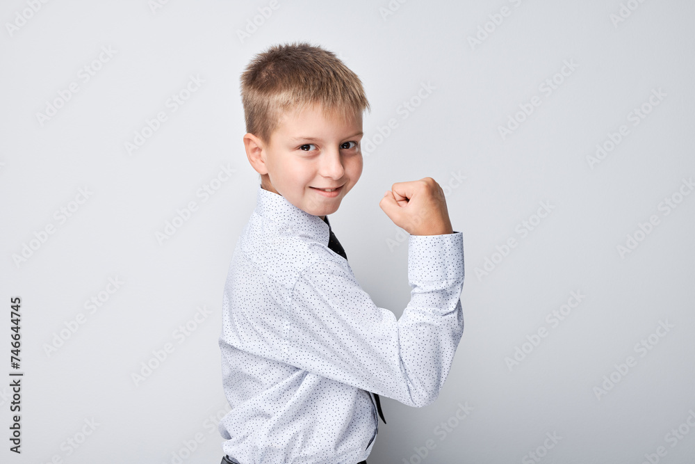 Confident young boy in white shirt showing muscles on plain background, strength and growth.