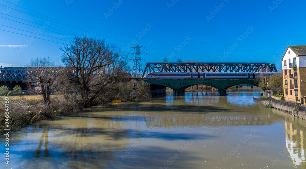 A view along the River Nene towards the historic cast iron railway bridge in Peterborough, UK on a bright sunny day