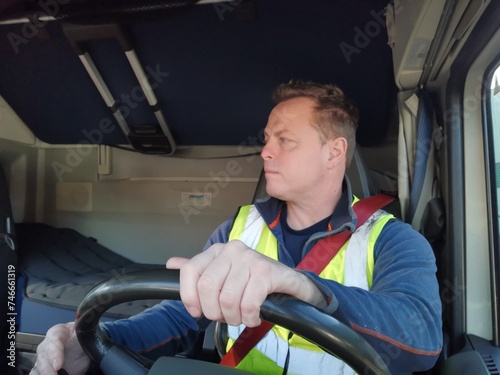 Truck Driver driving with high Visibility Vest and Red Seat Belt on, behind the Steering Wheel of a Semi Truck. interior Image. 