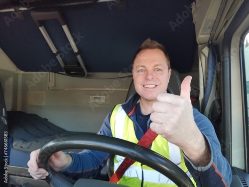 Truck Driver driving with high Visibility Vest and Red Seat Belt on, behind the Steering Wheel of a Semi Truck. interior Image, with the driver giving a Thumbs Up