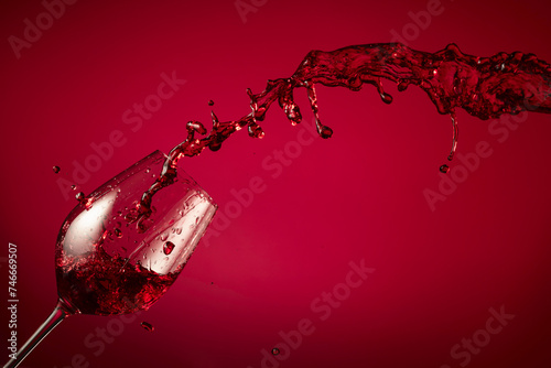 Glass and red wine splash on a red background.