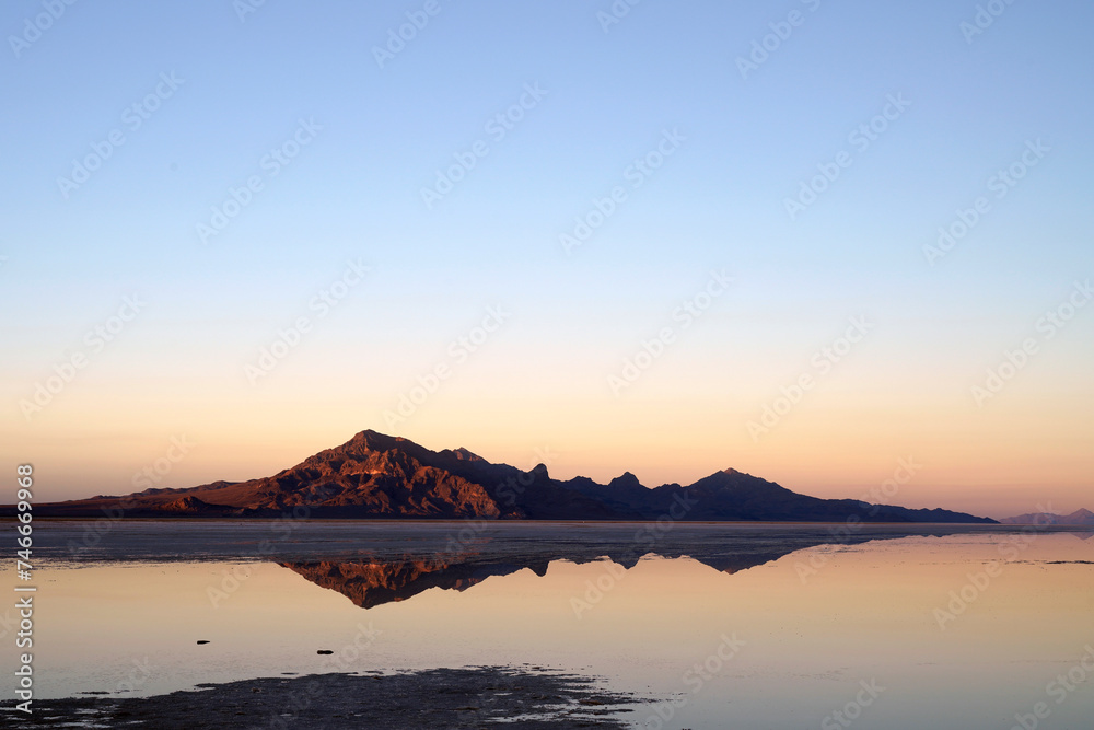 Sunset at Bonneville Salt Flats with beautiful water reflections in the salt lake and mountain silhouette in the background and blue sky near Wendover in Utah, United States