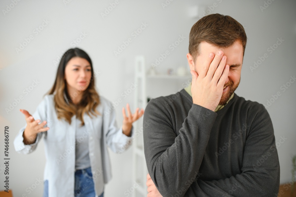 Couple arguing. Wife shouting to her desperate husband sitting on a couch in the living room at home Couple arguing. Wife shouting to her desperate husband sitting on a couch in the living room at home
