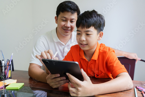Father helping his son doing homework and writing on tablet with