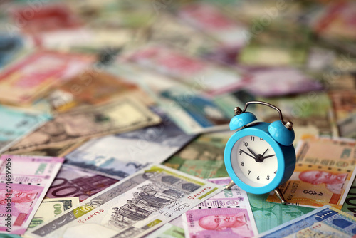 Small alarm clock on many banknotes of different currency. Background of time and money close up © mehaniq41