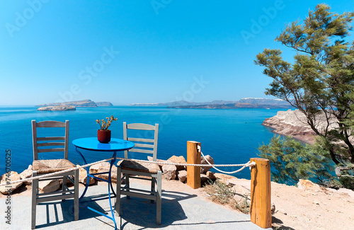 Greek gray chairs and blue table on a typical sunny terrace with a lovely view near the Lighthouse of Akrotiri, Santorini. Greek Islands, European Vacation.  © trattieritratti