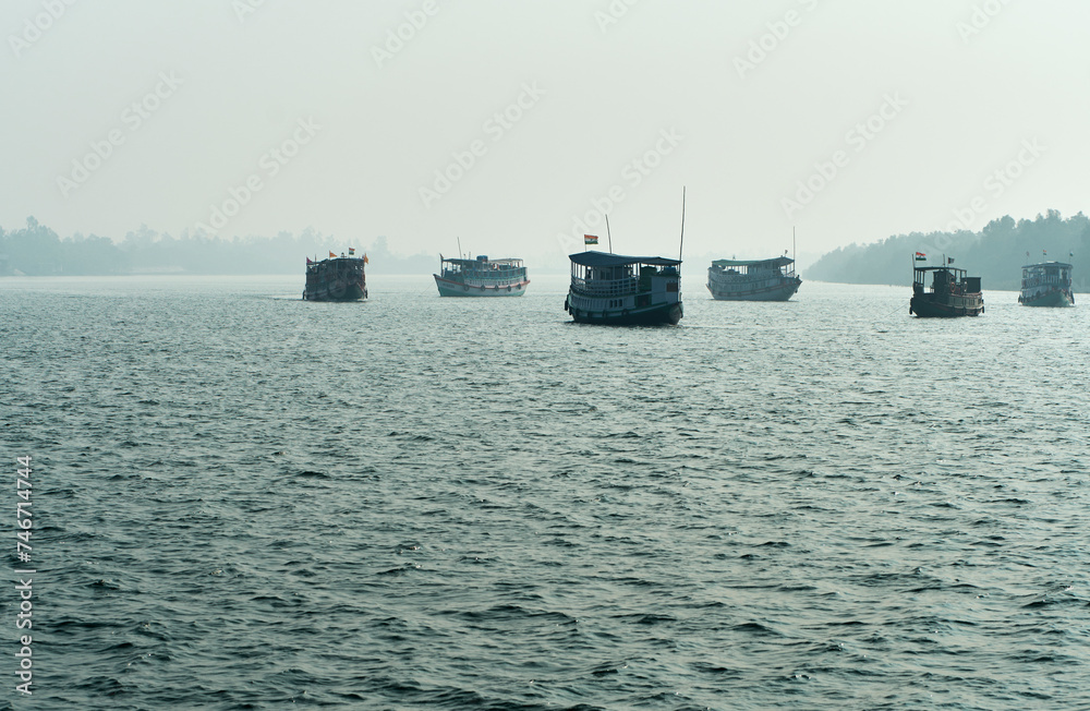 Silhouette of traditional tourist vessels and fishing boats cruising through vast waterbody at Sundarbans biosphere reserve in a foggy winter morning. Sundarbans is a popular ecotourism destination.