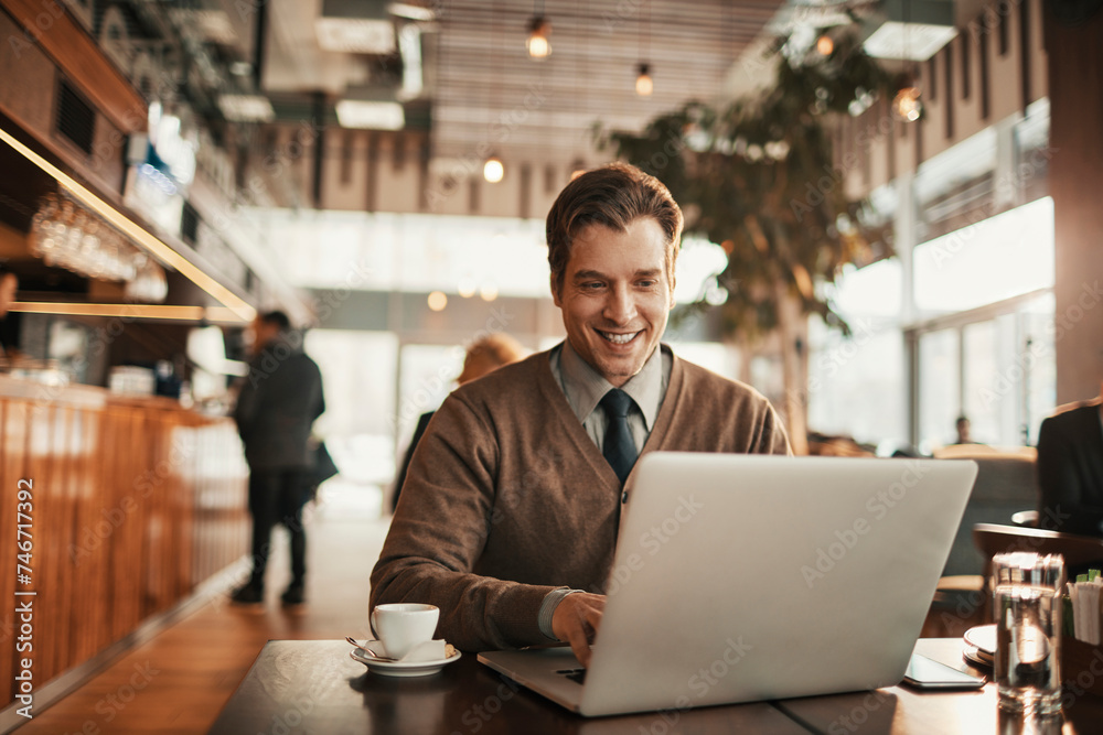 Young businessman using a laptop while enjoying coffee at an indoor cafe Young businessman using a laptop while enjoying coffee at an indoor cafe