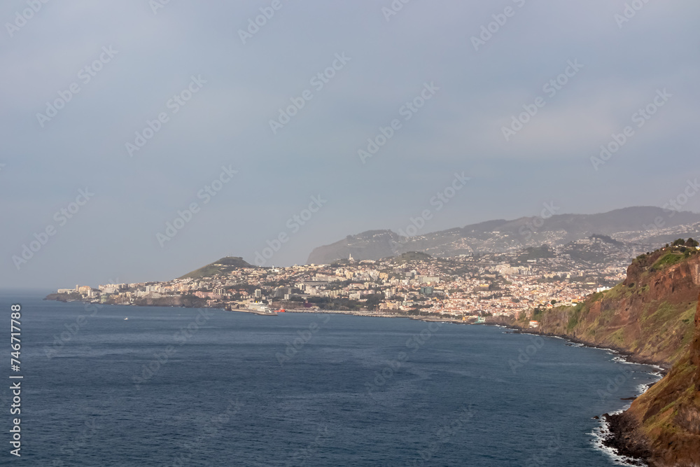 Panoramic view city of Funchal seen from Cristo Rei in Garajau, Madeira island, Portugal, Europe. Majestic coastline with steep cliffs along Atlantic Ocean. Travel destination on cloudy day. Seascape
