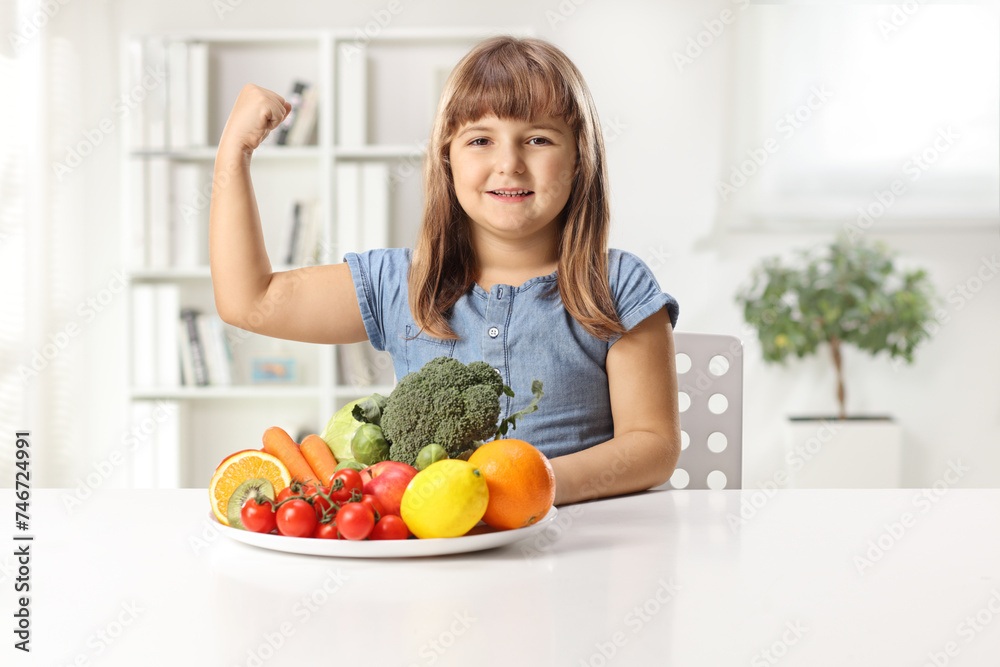 Happy little girl sitting with a plate of fruits and vegetables on a table