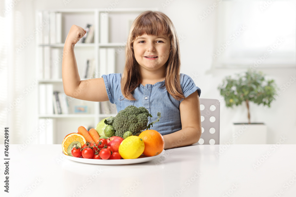 Happy little girl sitting with a plate of fruits and vegetables on a table Happy little girl sitting with a plate of fruits and vegetables on a table
