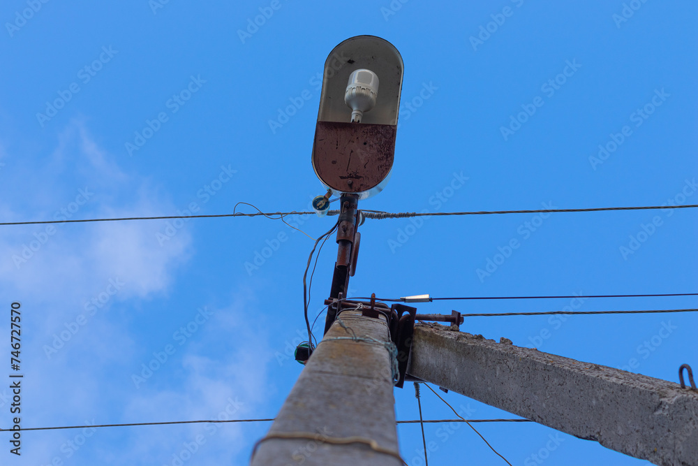 Obraz premium Old concrete lighting pole with a single lamp and wires against the sky. View from the bottom.