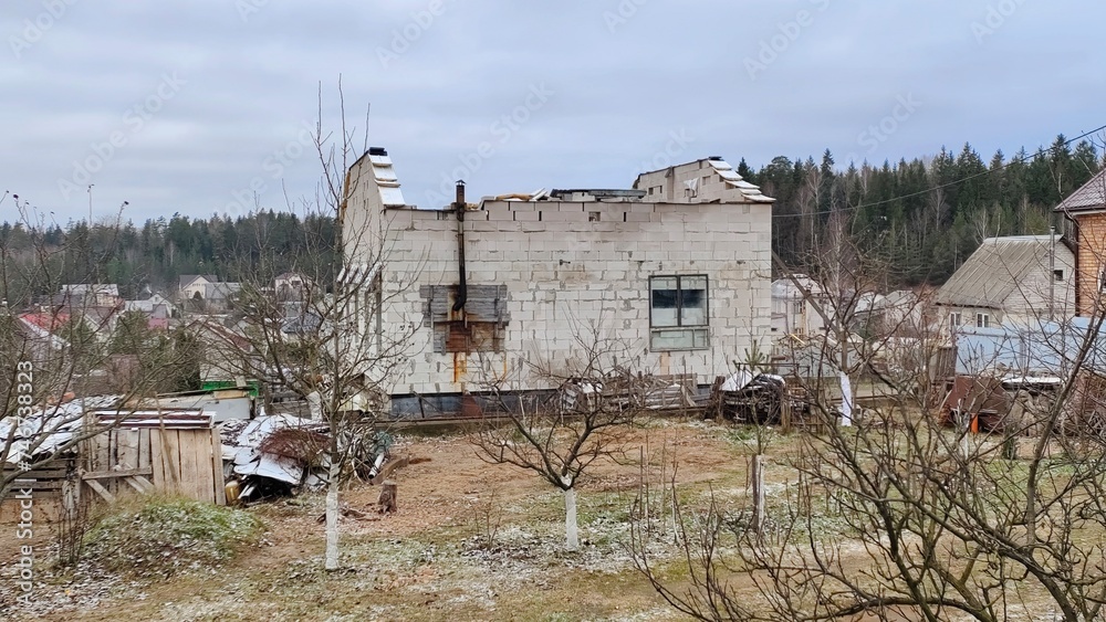 An old block house with no roof is surrounded by fruit trees and other buildings. There is a metal pipe sticking out of the wall. The house is in need of repair. Overcast and cold winter weather