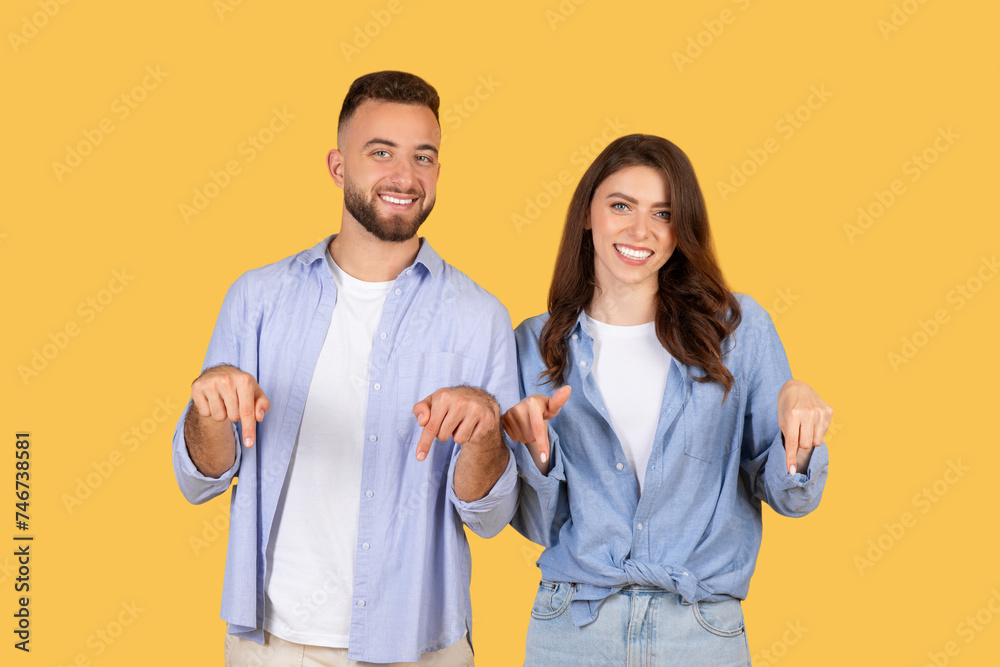 Cheerful duo in blue shirts pointing down with smiles Cheerful duo in blue shirts pointing down with smiles