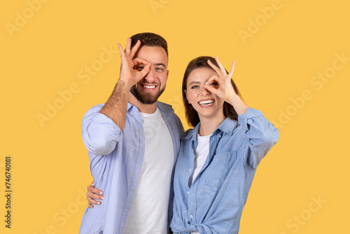 Playful european couple making fun gestures on yellow